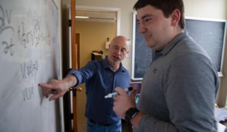 An instructor point to statistics on a white board as a student looks on